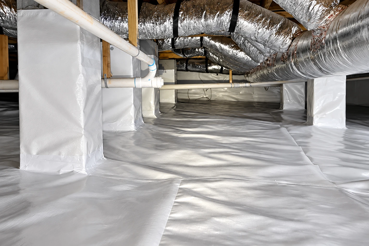 Crawl space with a white vapor barrier covering the floor and wrapped around support piers beneath shiny ductwork.