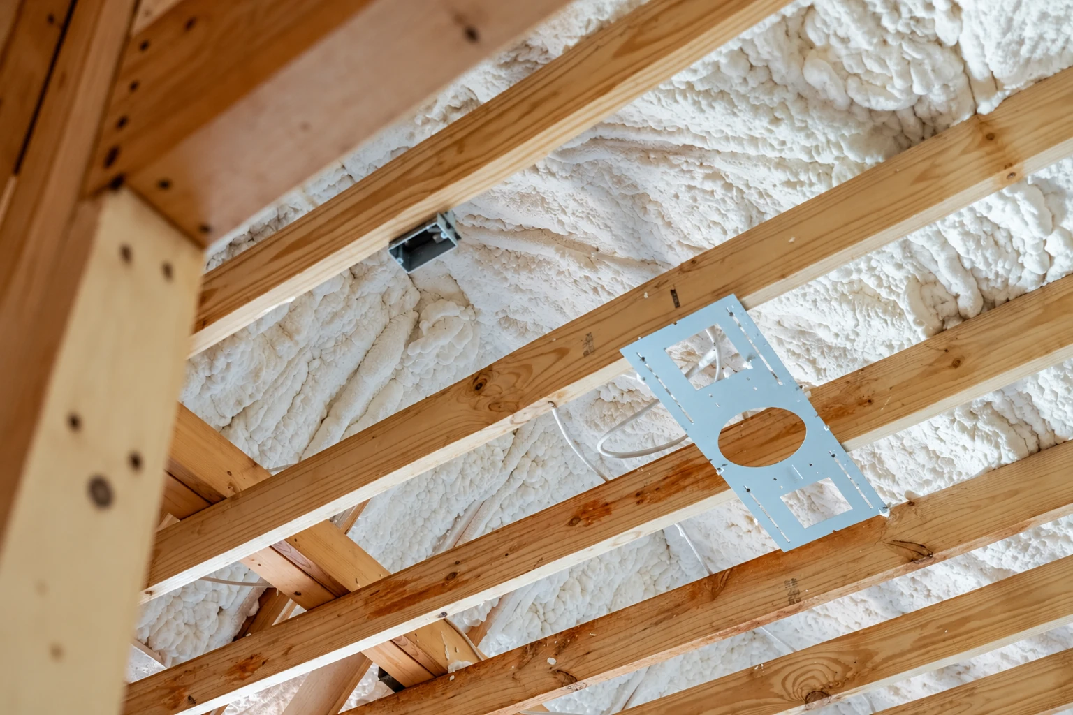 Open-cell spray foam insulation covers the underside of a roof between exposed wooden rafters.