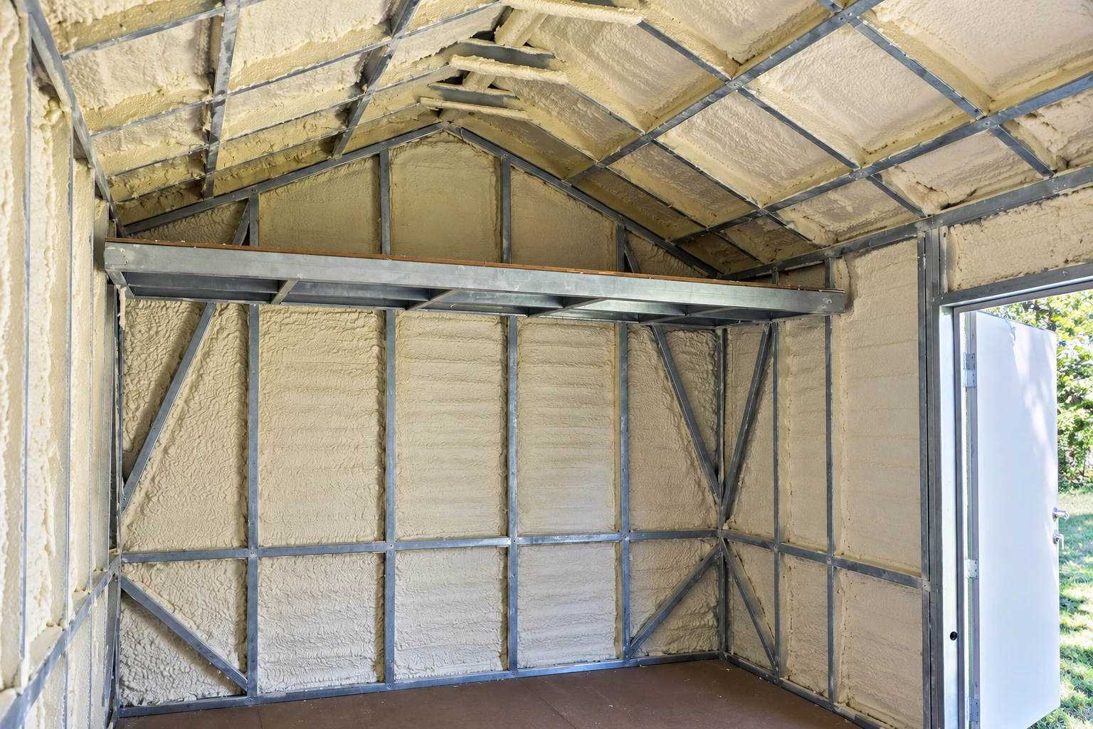 Spray foam insulation fills the walls and sloped ceiling of a metal-framed room beside an open doorway.