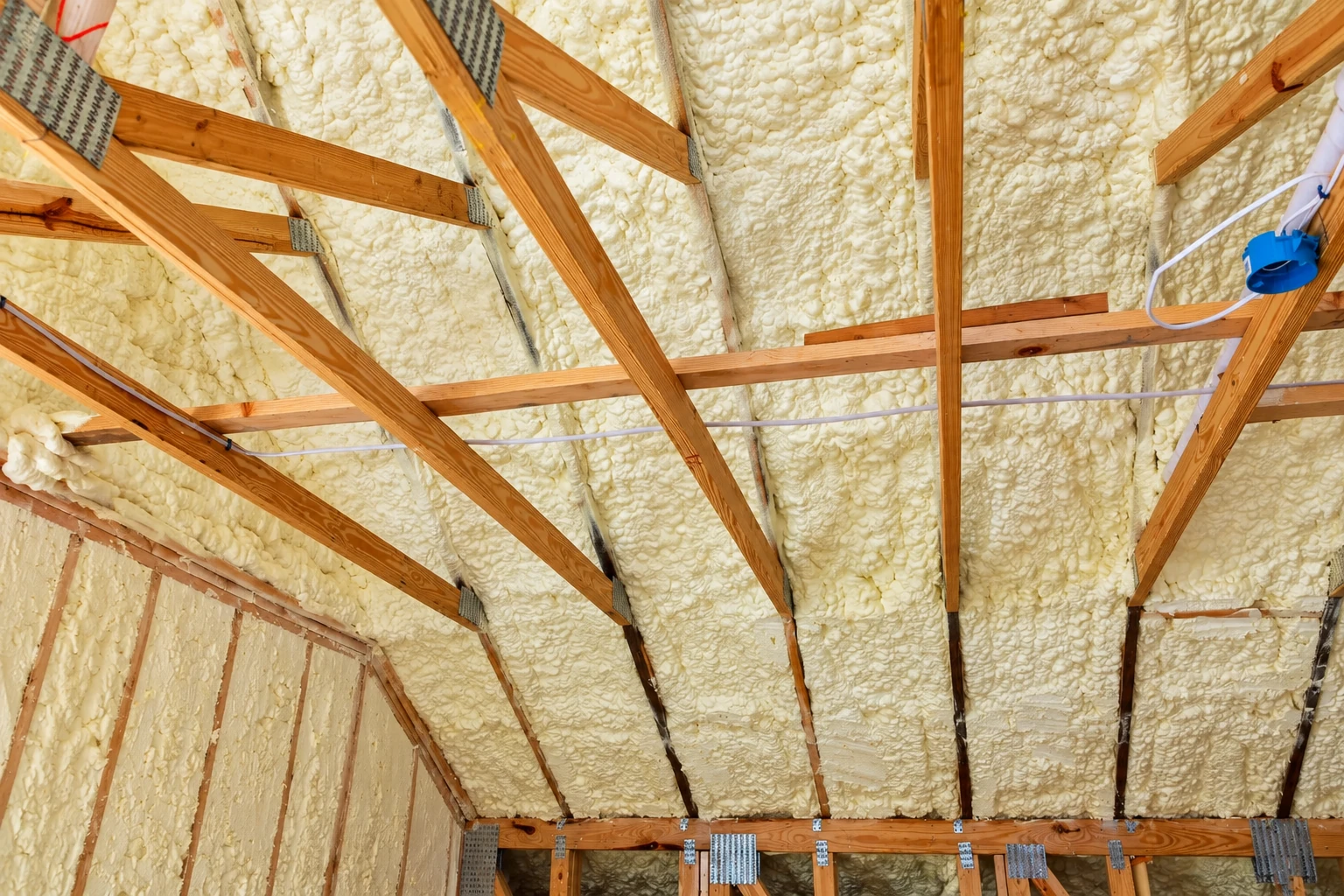 Spray foam fills the roof framing between exposed wooden rafters, with wiring running across the ceiling.